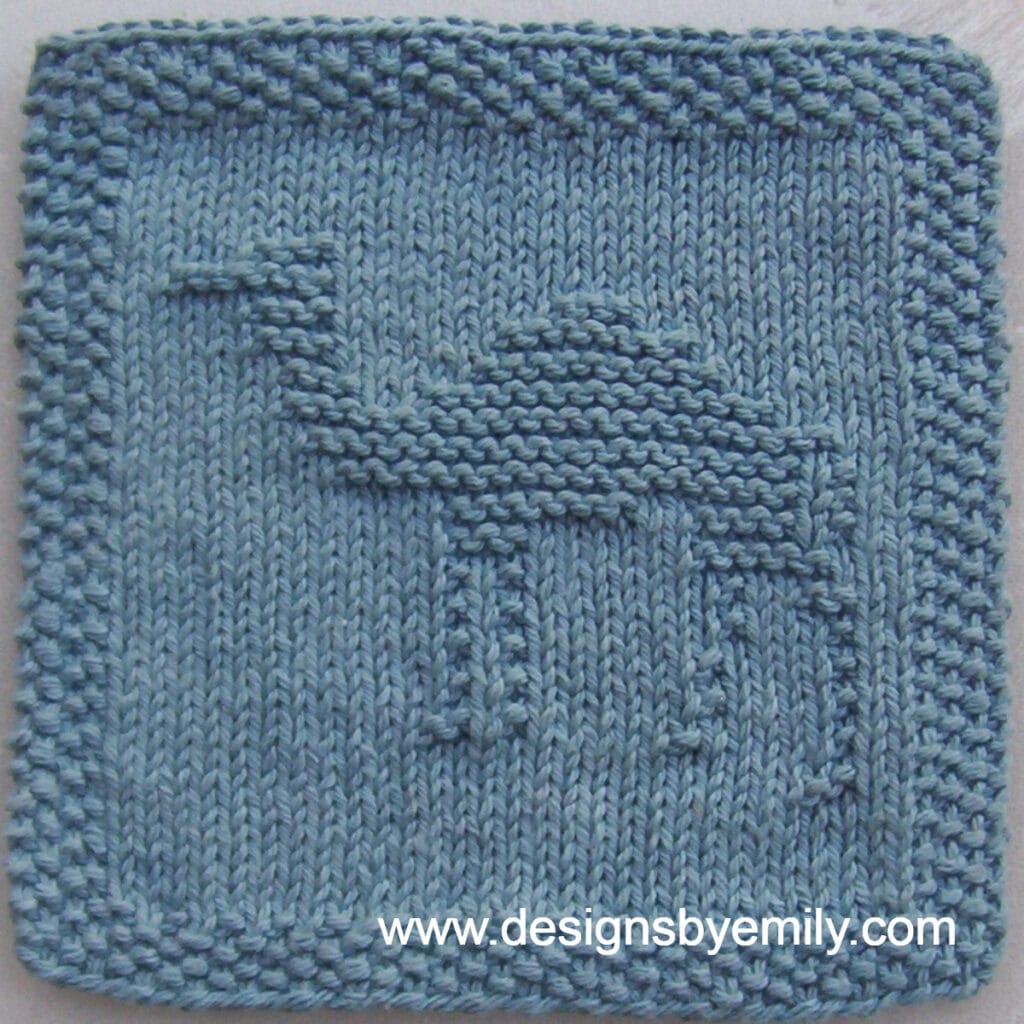 Camel Knit Dishcloth: A handmade knit dishcloth square in blue yarn featuring a camel in the center facing toward the left. The design is created in garter stitch using knit and purl stitches on a stockinette background.