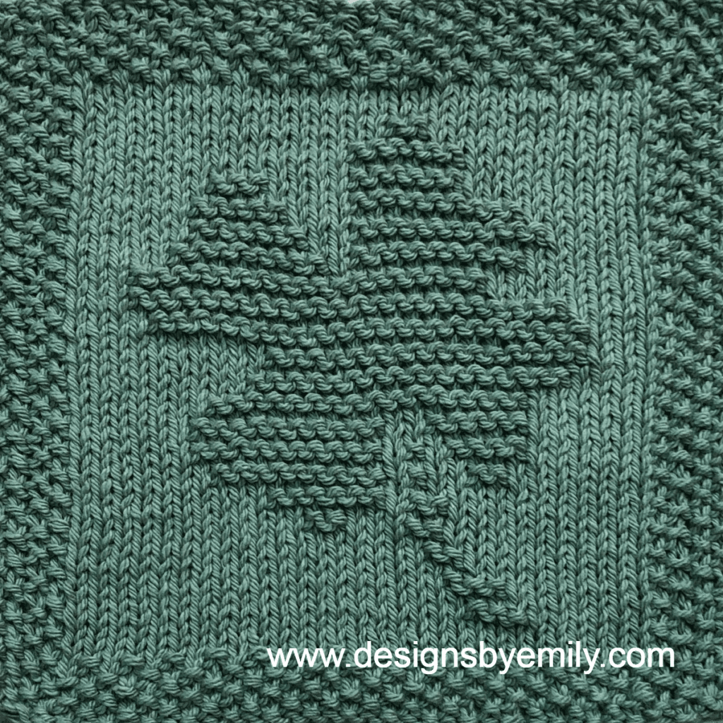 Four-Leaf Clover Knit Dishcloth: A handmade knit dishcloth square in green yarn featuring a four-leaf clover with its stem angled toward the right. The design is created in garter stitch using knit and purl stitches on a stockinette background.