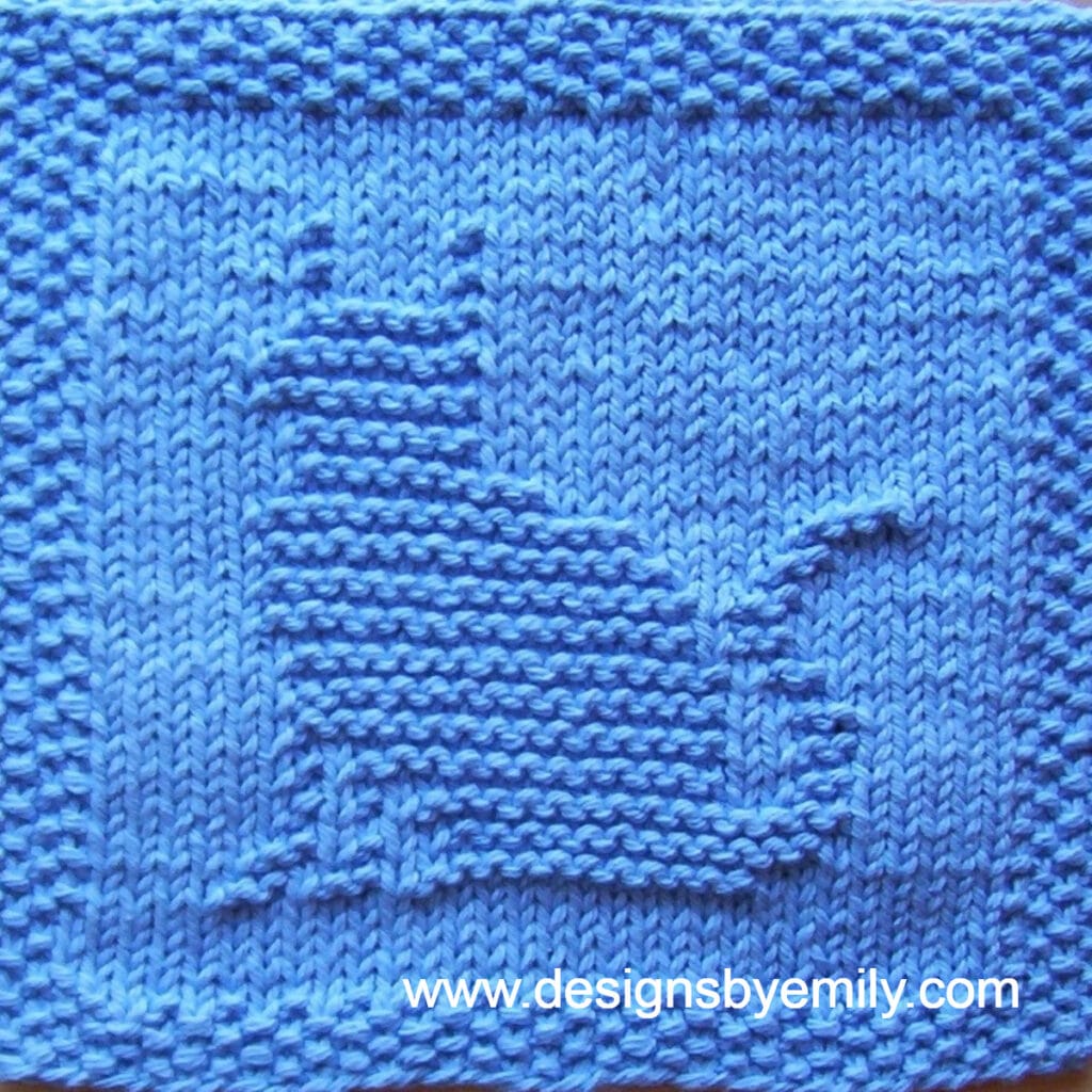 Kitty Cat Knit Dishcloth: A handmade knit dishcloth square in blue yarn featuring a cat sitting and facing toward the left. The design is created in garter stitch using knit and purl stitches on a stockinette background.