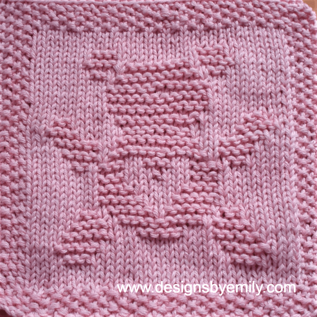 Teddy Bear Love Knit Dishcloth: A handmade knitted dishcloth square in light pink yarn featuring a cute teddy bear with its arms and legs spread out and a heart on its belly. The design is created in garter stitch using knit and purl stitches on a stockinette background.